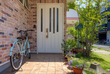 住宅の白い扉の玄関に置いてある水色の自転車と花