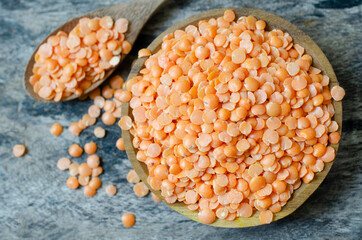 Top view of dry organic red lentil seeds in wooden bowl and spoon on grunge background. Concept of healthy food ingredient or agricultural product concept