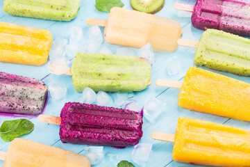 Poster - Various fruit popsicles are placed on the blue wooden board background, kiwi popsicles, orange popsicles, dragon fruit popsicles, cantaloupe popsicle