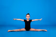 a little gymnast in a black swimsuit does the splits on a blue background with a place for text