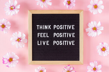 Wall Mural - Think positive, feel positive, live positive. Motivational quote on letter board and flowers on pink background. Concept inspirational quote of the day. Flat lay Top view