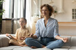 © fizkes - Peaceful mother with little daughter relaxing meditating on couch together, calm young mom teaching preschool girl practicing doing yoga exercise at home, family meditation, healthy lifestyle concept