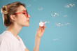 © New Africa - Young woman blowing soap bubbles on light blue background, space for text