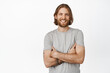 © Cookie Studio - Image of handsome bearded guy with blond hairstyle, cross arms on chest, smiling white teeth, looking happy, standing in grey t-shirt against white background