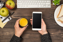 First Person Top View Photo Of Hands Holding Smartphone And Glass Of Juice Over Plate With Toasts Keyboard Mouse Apples Plant And Stationery On Isolated Dark Wooden Table Background With Blank Space