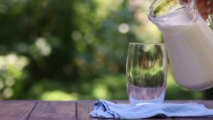 Wall Mural - milk pouring from jug into glass outdoors