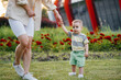 © Andrii - A young cute mother helps and teaches her little son to take his first steps during sunset in the park on the grass.