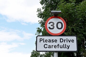 UK road sign 30 mph Please Drive Carefully... Blue cloudy sky.