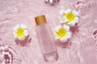 Glass bottle with plumeria flowers in rose water background. Splash of water.