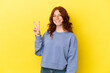 © luismolinero - Teenager reddish woman isolated on yellow background smiling and showing victory sign
