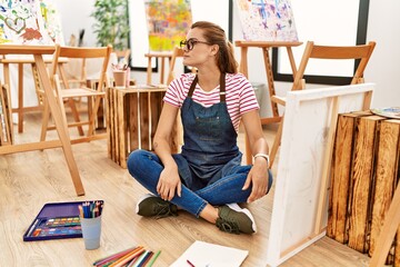 Sticker - Young brunette woman at art studio sitting on the floor looking to side, relax profile pose with natural face with confident smile.