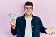 Young hispanic man holding 100 romanian leu banknotes celebrating achievement with happy smile and winner expression with raised hand