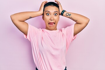 Wall Mural - Beautiful hispanic woman with short hair wearing casual pink t shirt crazy and scared with hands on head, afraid and surprised of shock with open mouth