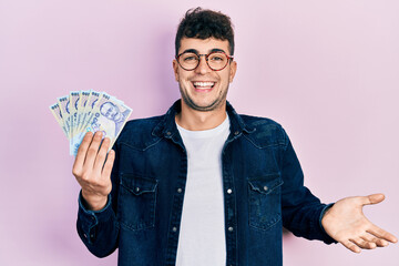 Canvas Print - Young hispanic man holding 100 romanian leu banknotes celebrating achievement with happy smile and winner expression with raised hand