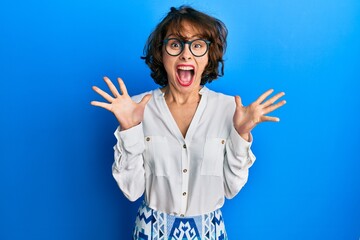 Sticker - Young brunette woman wearing casual clothes and glasses celebrating crazy and amazed for success with arms raised and open eyes screaming excited. winner concept