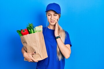 Sticker - Young caucasian woman wearing courier uniform with groceries from supermarket touching mouth with hand with painful expression because of toothache or dental illness on teeth. dentist concept.