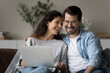 Happy millennial couple enjoying dating at home, watching and discussing movie on laptop, relaxing on couch, talking, laughing. Husband and wife making paying bills, paying mortgage, insurance fees