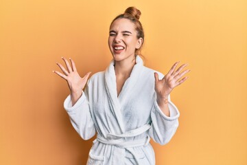 Canvas Print - Young blonde woman wearing bathrobe celebrating mad and crazy for success with arms raised and closed eyes screaming excited. winner concept