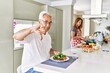 Middle age hispanic couple eating healthy meal at home with angry face, negative sign showing dislike with thumbs down, rejection concept