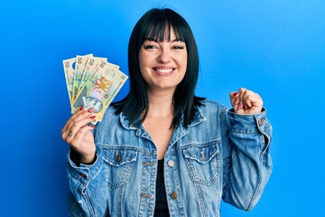 Sticker - Young hispanic woman holding 50 romanian leu banknotes screaming proud, celebrating victory and success very excited with raised arm