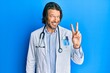 © Krakenimages.com - Middle age handsome man wearing doctor uniform and stethoscope smiling with happy face winking at the camera doing victory sign. number two.