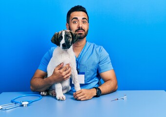 Sticker - Handsome hispanic veterinary man with beard checking dog health looking sleepy and tired, exhausted for fatigue and hangover, lazy eyes in the morning.