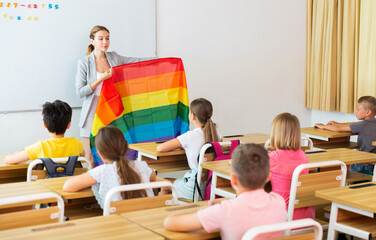 Young smiling woman teacher explaining lgbt theme to children during class in primary school