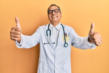 Poster - Middle age indian man wearing doctor coat and stethoscope approving doing positive gesture with hand, thumbs up smiling and happy for success. winner gesture.