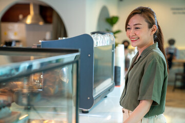 Wall Mural - Asian woman coffee shop employee barista working at cafe. Smiling female waitress cashier taking order coffee and bakery from customer. Small business owner and part time job working concept