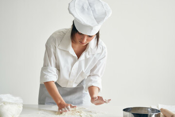 Wall Mural - woman baker in chef uniform rolls out dough flour professional cooking