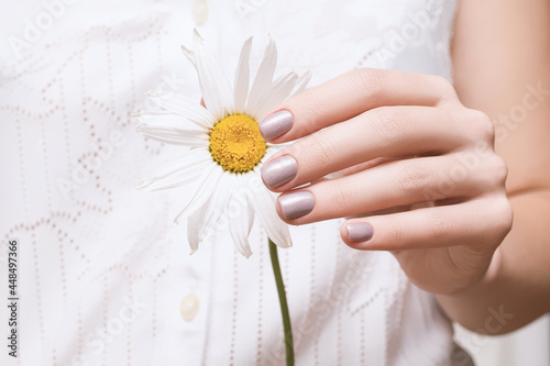 Female hand with glitter pearl nail design. Female hand hold yellow chamomile flower. Glitter pearl perfect manicure