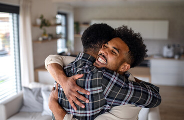 Wall Mural - Young happy adult brothers in kitchen indoors at home, hugging.