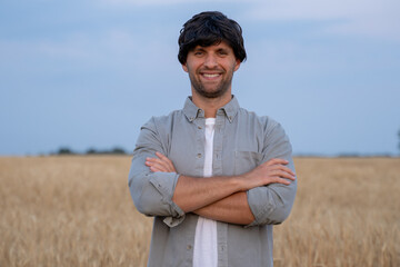 Wall Mural - Male farmer crosses his arms and looks at the camera against the background of a wheat field