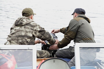 Wall Mural - Two Russian men start an outboard boat motor on the transom of the boat, emergency engine start with spare rope