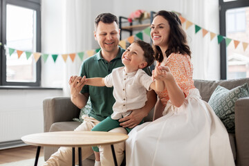 Wall Mural - family, holidays and people concept - portrait of happy mother, father and little son sitting on sofa at home party