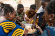 Group of coulorfully dressed black girls sitting around a big metal bowl, sharing a typical African meal made out of rice and vegetables