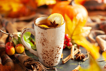 Autumn or winter spice tea in mug with seasonal fruits, berries, pumpkin and leaves on wooden table.