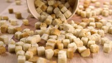 Wheat toasted cube croutons fall on a wooden board in slow motion from a paper cup. Macro shot