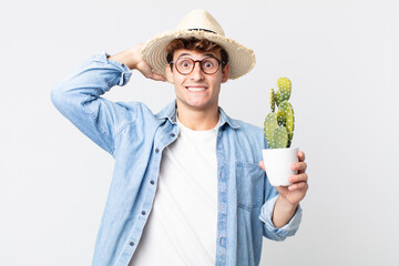 young handsome man feeling stressed, anxious or scared, with hands on head. farmer holding a decorative cactus