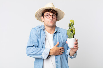 Wall Mural - young handsome man shrugging, feeling confused and uncertain. farmer holding a decorative cactus