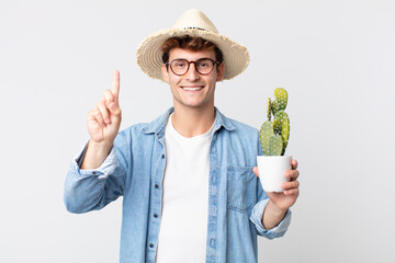 Wall Mural - young handsome man smiling and looking friendly, showing number one. farmer holding a decorative cactus