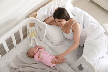 Wall Mural - Young mother resting near crib with sleeping newborn baby at home, above view