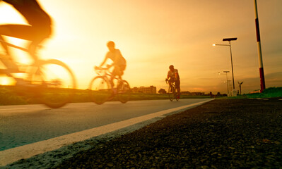 Blur photo sports man ride bicycles with speed motion on the road in the evening with sunset sky. Summer outdoor exercise for healthy and happy life. Cyclist riding mountain bike on bike lane. Team.