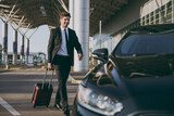 Full body bottom view young traveler businessman young man in black dinner suit going walk outside at international airport terminal with suitcase to car booking taxi Air flight business trip concept