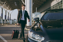Full Body Bottom View Young Traveler Businessman Young Man In Black Dinner Suit Going Walk Outside At International Airport Terminal With Suitcase To Car Booking Taxi Air Flight Business Trip Concept