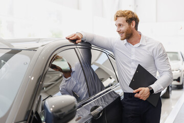 Wall Mural - Man pensive customer male buyer client in white shirt hold clipboard paper document lean on car choose auto want buy new automobile in showroom vehicle dealership store motor show indoor Sale concept