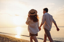 Back Rear View Young Happy Couple Two Friends Family Man Woman 20s In White Shirt Clothes Hold Hands Walk Stroll Together At Sunrise Over Sea Beach Ocean Outdoor Exotic Seaside In Summer Day Evening.