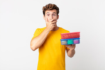 Wall Mural - young handsome man covering mouth with hands with a shocked and holding lunch boxes