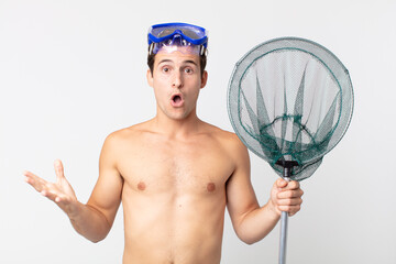 Wall Mural - young handsome man feeling extremely shocked and surprised with goggles and a fishing net