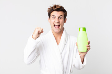 Wall Mural - young handsome man feeling extremely shocked and surprised with bathrobe and holding a shampoo bottle